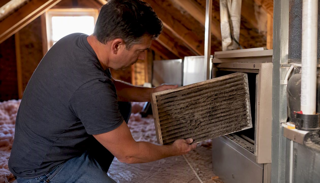 Hands pulling dirty air filter from HVAC unit