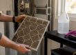 Hands removing dirty HVAC filter indoors
