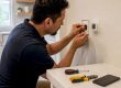 Hands wiring smart thermostat on home wall