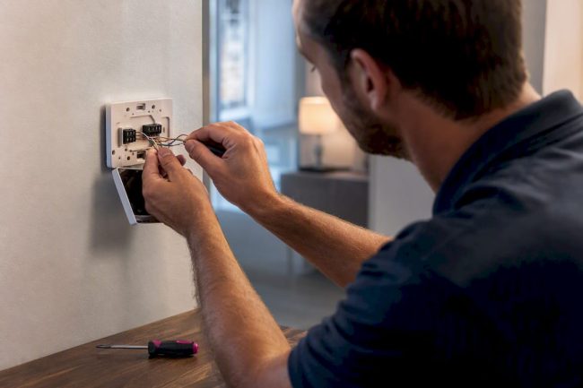 Technician connecting thermostat wiring at a wall