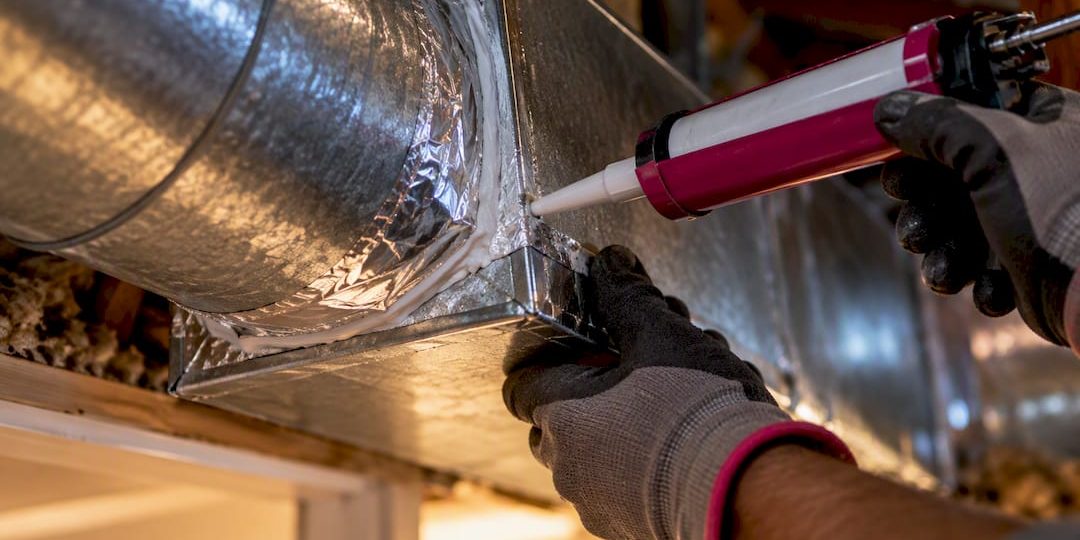 1790332885169_Technician-sealing-an-exposed-duct-junction Technician sealing an exposed duct junction