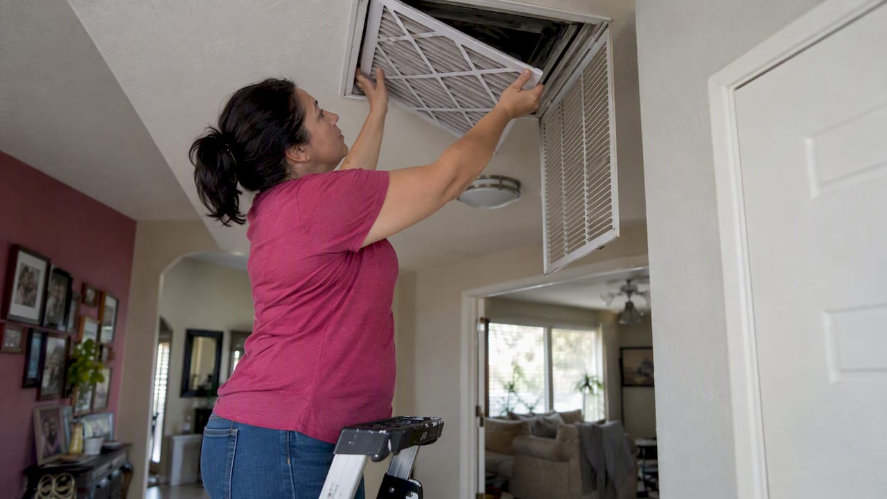 Homeowner changing a ceiling return air filter