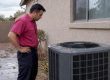 Technician inspecting a storm-hit AC condenser