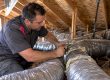 A technician inspects aging flexible attic ducts